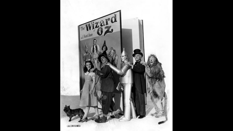 Judy Garland as Dorothy Gale, Ray Bolger as the Scarecrow, Jack Haley as the Tin Man, Frank Morgan as the Wizard, Bert Lahr as the Cowardly Lion and Terry as Toto with an oversized prop book of "The Wizard of Oz."