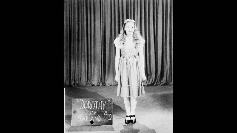 A wardrobe test shot of Judy Garland in a rejected Dorothy costume with a blonde wig.