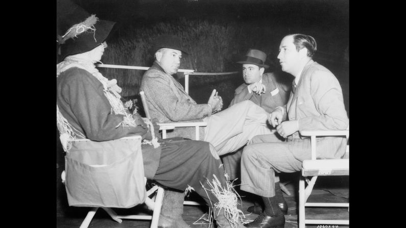 Ray Bolger in costume as the Scarecrow, seated with director Victor Fleming, choreographer Bobby Connolly and producer Mervyn LeRoy.