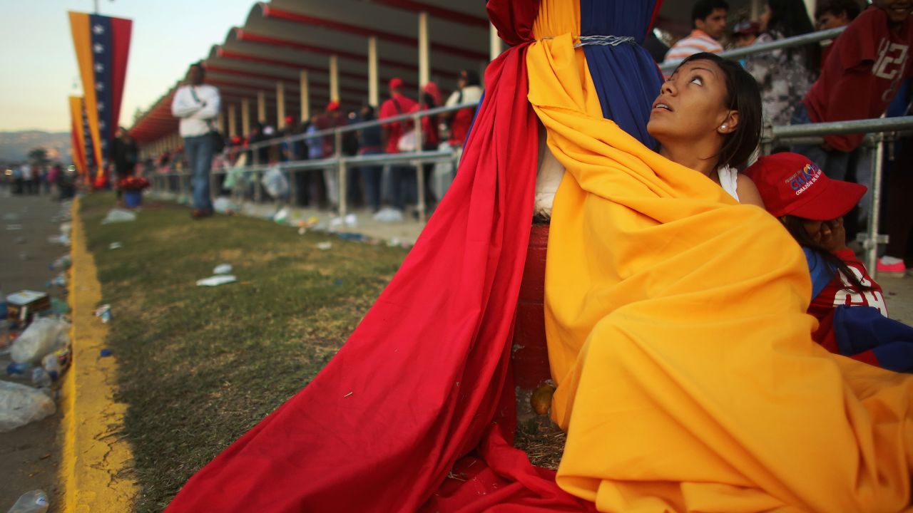 A woman wraps up in Venezuela's flag to stay warm as she and others wait in line before the start of Chavez's funeral.