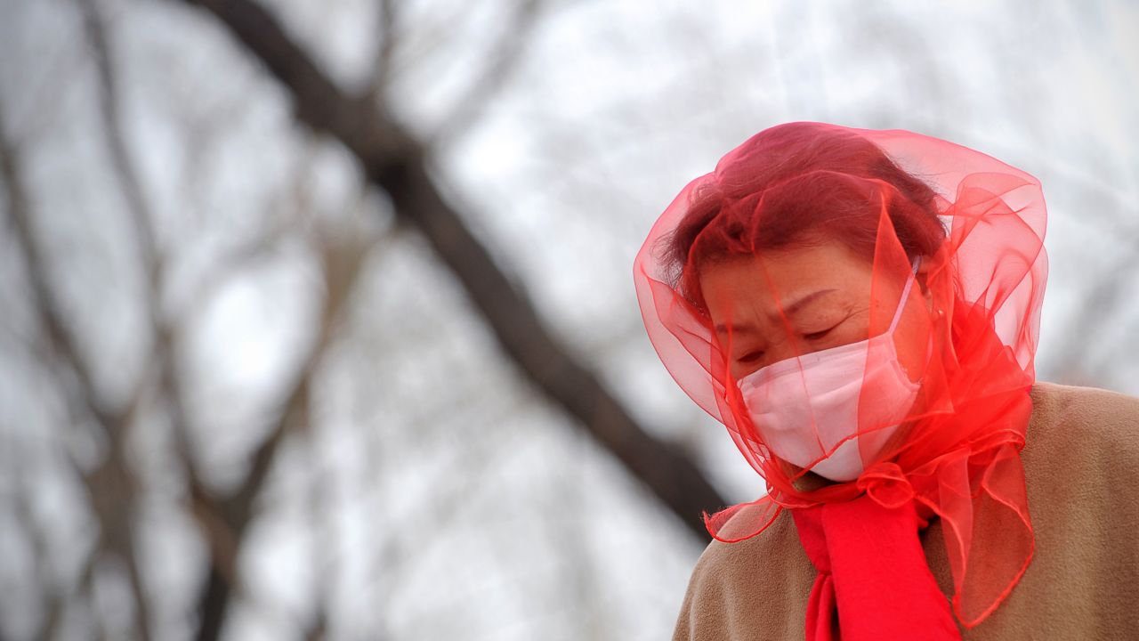 A Chinese woman covers her head with a scarf as she walks near Tiananmen Square in Beijing on Saturday, March 9, as strong winds and dust storms swept the Chinese capital.