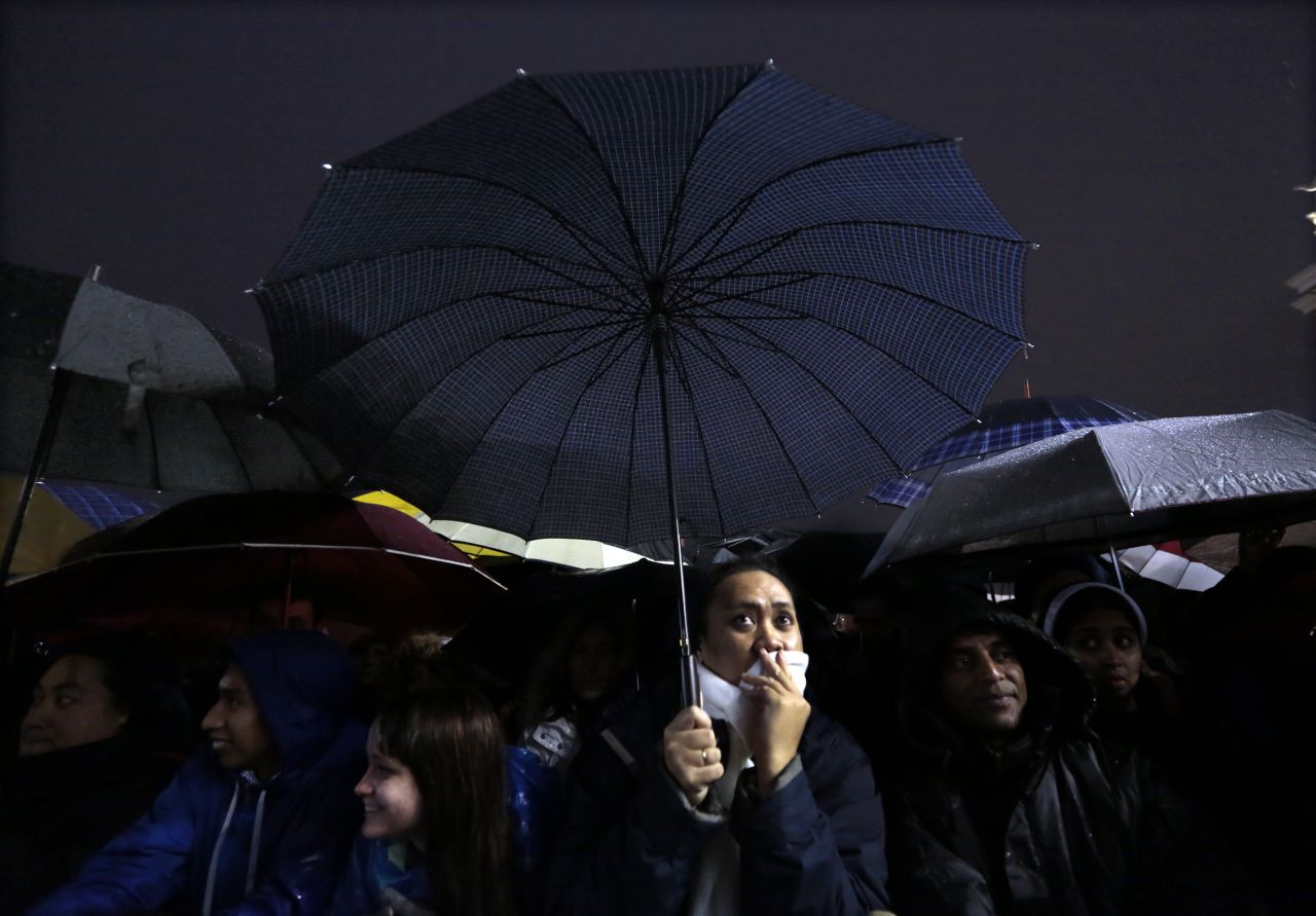 People under umbrellas react to the news while waiting for the new pope to appear.