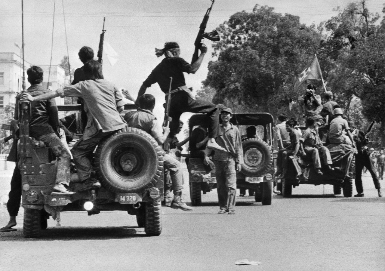 Khmer Rouge guerilla soldiers wearing black uniforms drive atop jeeps through a street of Phnom Penh on the day Cambodia fell under their control in April 1975. 