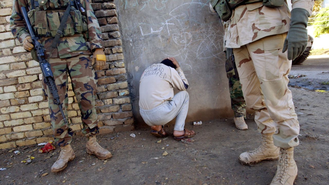 A bound Iraqi informer, with his name inked in English across his back, crouches beside soldiers in the 4th Infantry Division after providing outdated information during a morning raid in in Samarra on December 19, 2003.