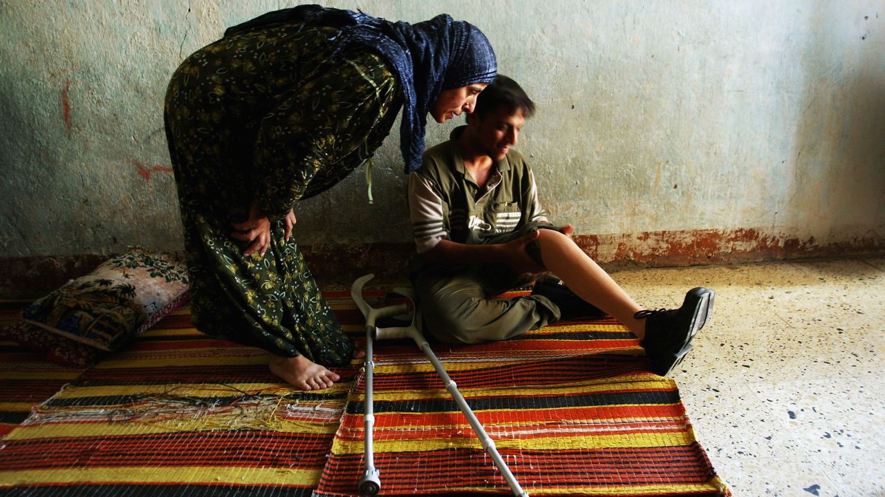 At home in Baghdad with his new prosthetic leg, Ahsan Hameed, 20, sits while his aunt looks it over on July 17, 2004. He lost his left leg above the knee to a stray bullet in April.