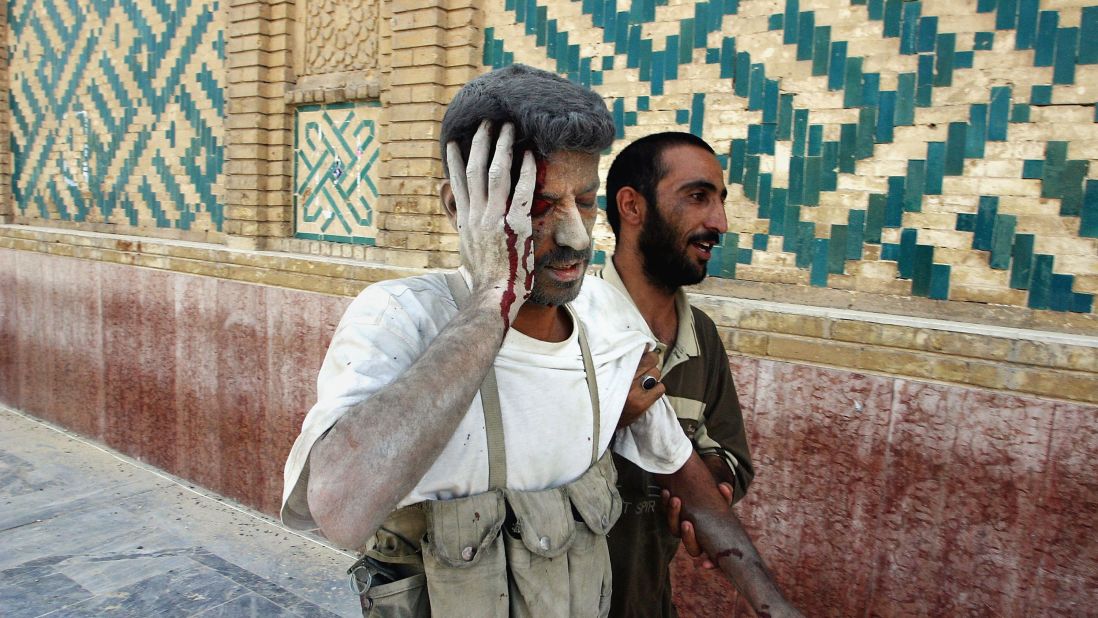 An Iraqi militia member injured in a U.S. airstrike in Najaf is assisted by one of his comrades on August 24, 2004. They were walking past the shrine of Imam Ali to make their way to a militia hospital.