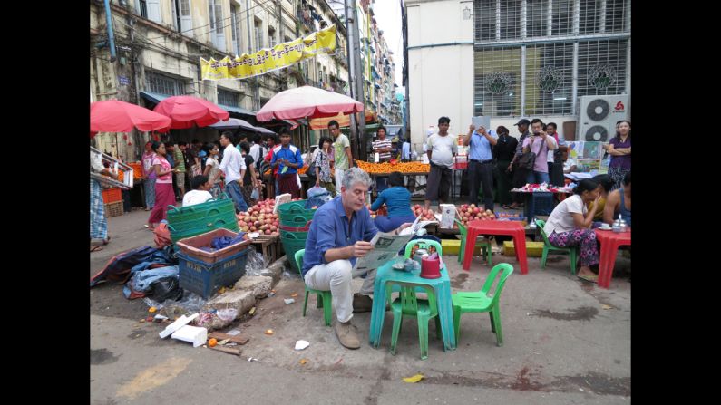 Bourdain reads a newspaper next to the local market in Yangon.
