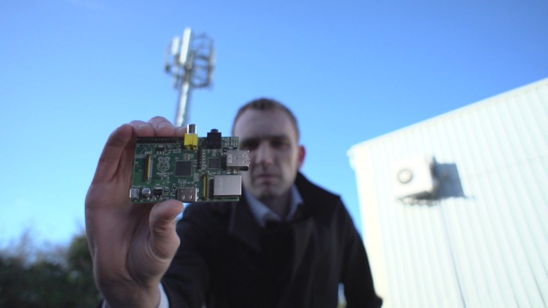 Alastair Smith, a wireless technology expert at PA Consulting Group, holds up a Raspberry Pi in front of a cell phone tower. The team created a private mobile-phone network by connecting the RPi, a $25 singleboard computer, to a radio interface.