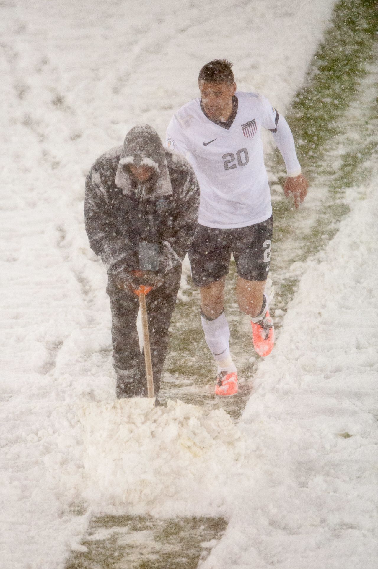 U.S. midfielder Geoff Cameron lends a hand as an official attempts to clear snow off the pitch markings.