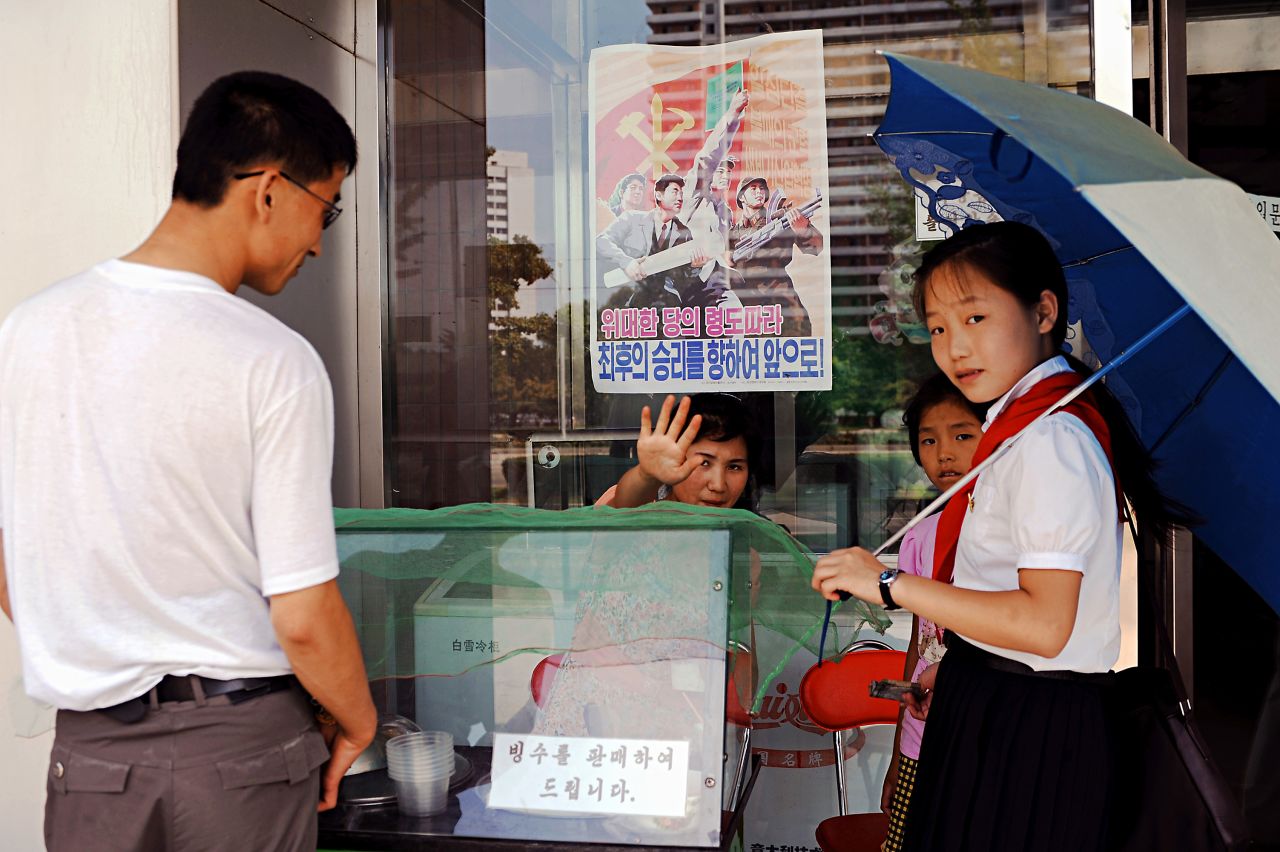My visit to North Korea coincided with hot summer weather. Here, people queue in front of an ice cream vendor in Pyongyang. The ice cream consists of only water, milk and sugar, but demand was high on that warm day. Behind the stall, a propaganda poster hangs on the window.