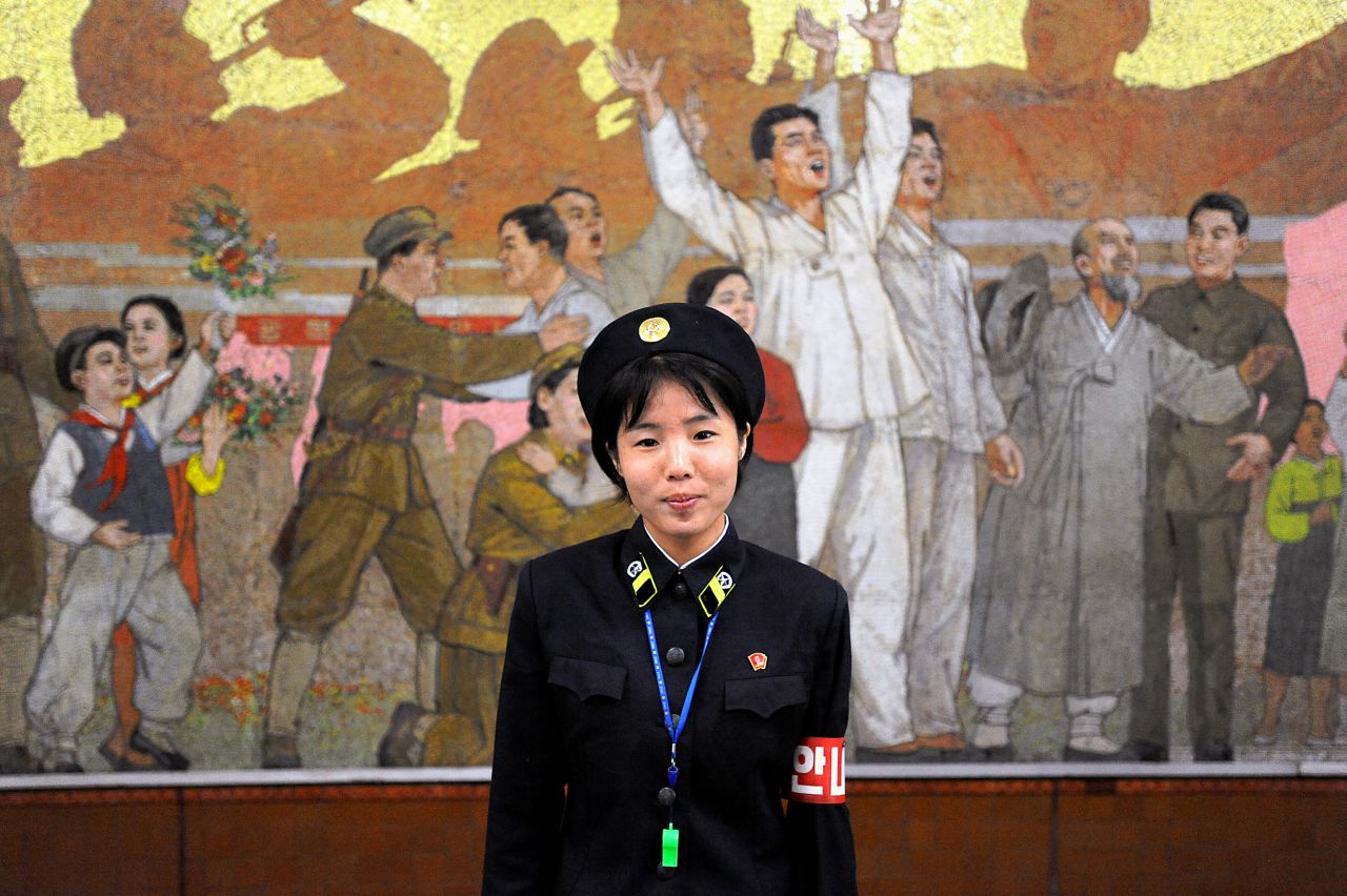 A metro guard poses in front of a propaganda mosaic inside one of the city's metro stations. Platform guards make sure metro traffic runs smoothly, warn people not to stand too close to the tracks and signal to train conductors when it's clear for departure.