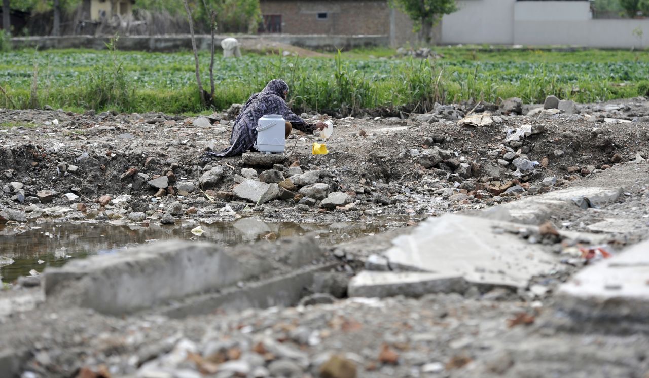 A Pakistani woman fills a container with water at the site of the demolished compound on April 25, 2012.