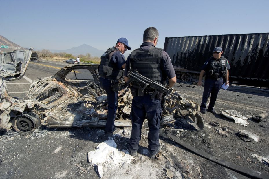 Mexican federal police officers inspect the charred wreckage of a car used to make a barricade blocking the Apatzingan-Uruapan road in Michoacan on December 11, 2010. Gunmen from the La Familia drug cartel blocked several roads in the state during a confrontation with the federal police, according to the state government.