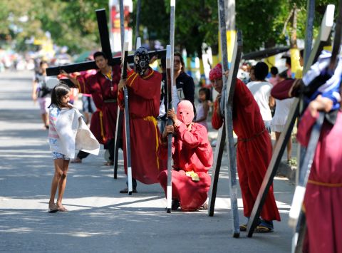 A girl watches penitents carrying wooden crosses taking a rest along a road during a ceremony in Angeles City, Pampanga.