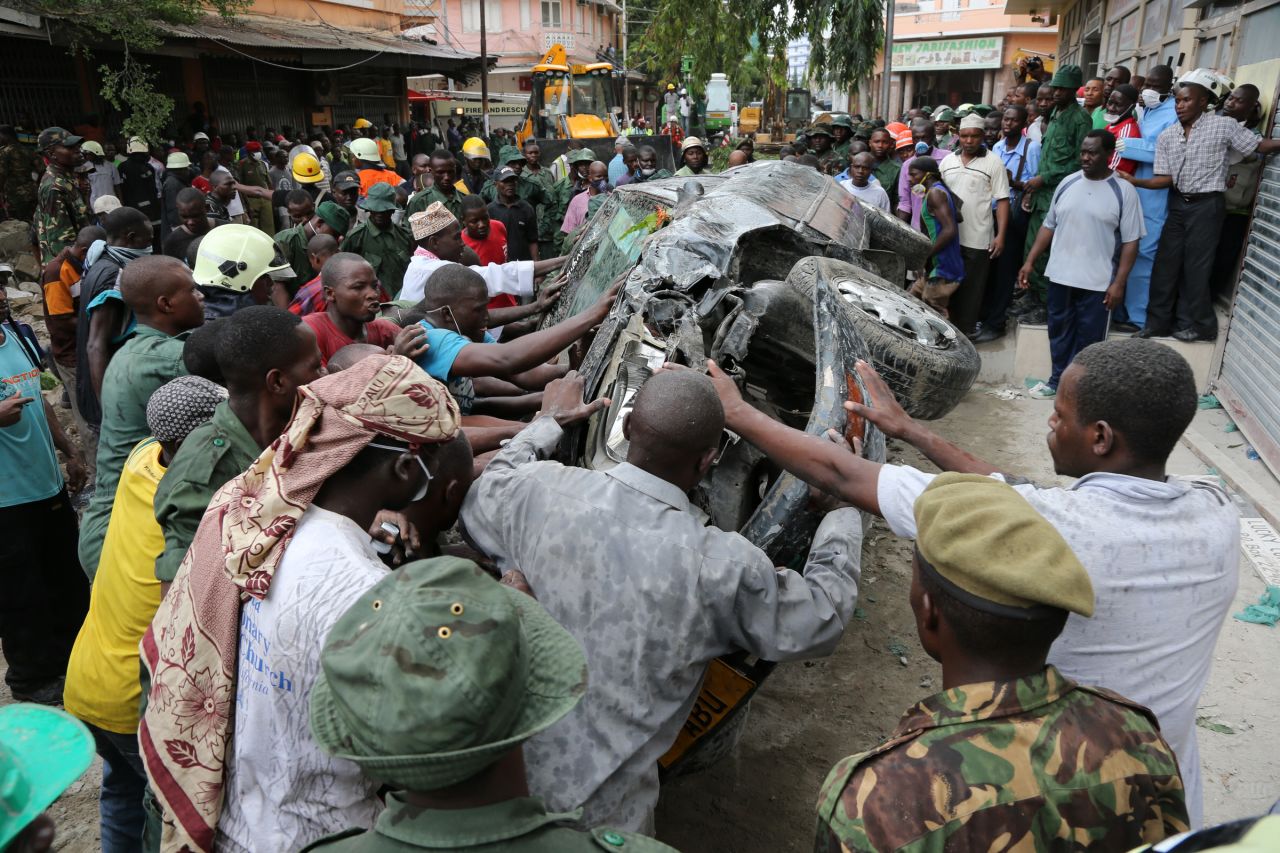 Rescuers and bystanders move a car smashed during the collapse.