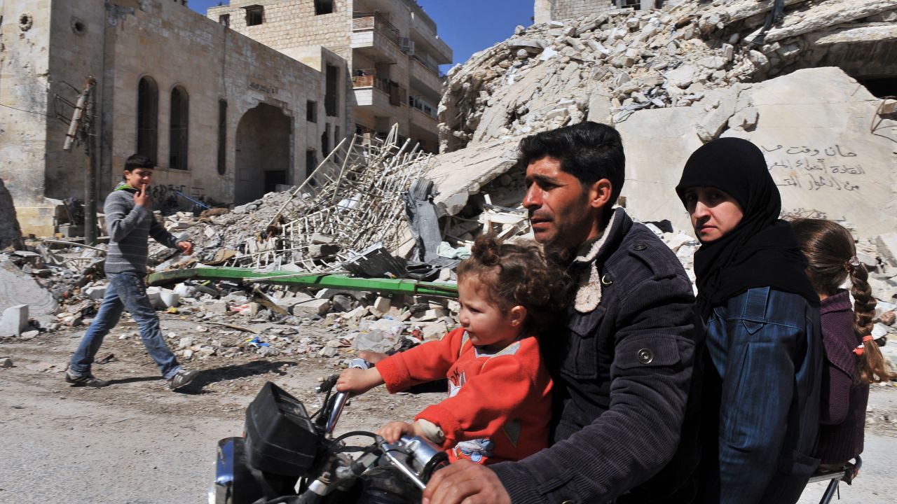 A Syrian man and his family drive past damaged buildings in Maarat al-Numan, on Wednesday, March 20.