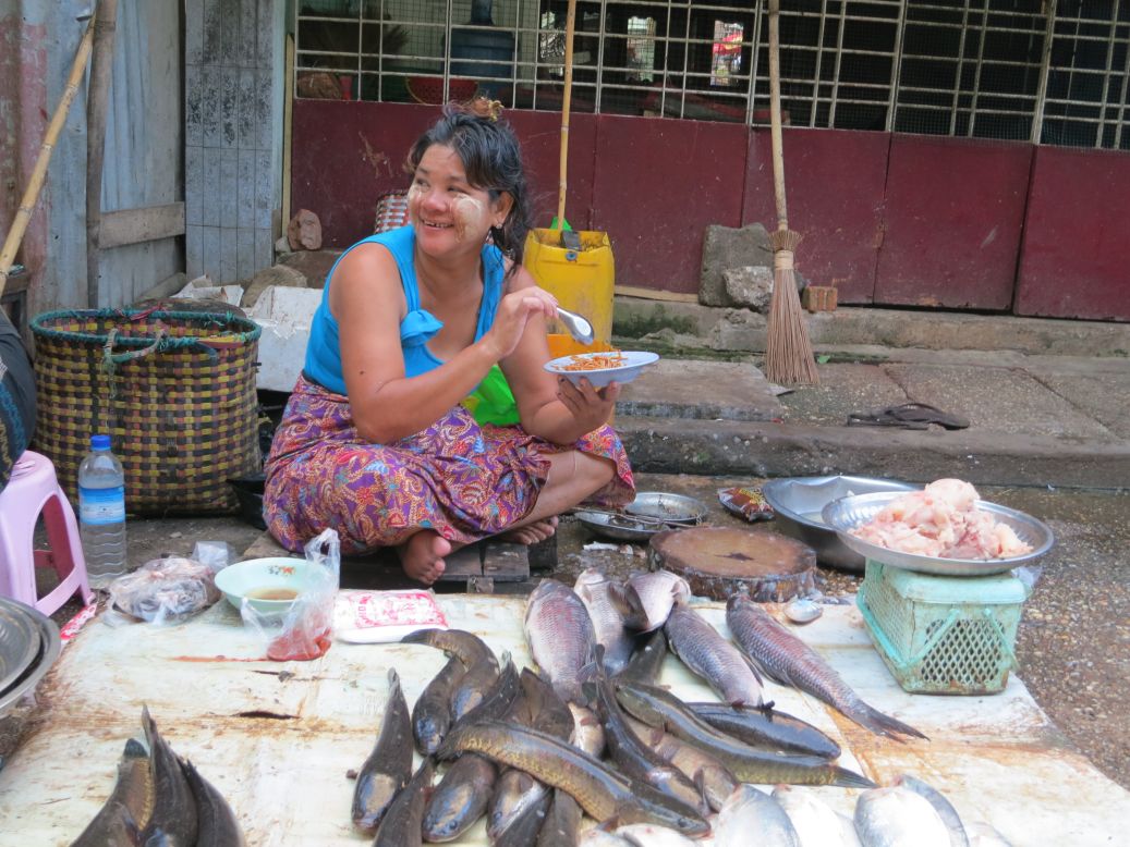 A fish vendor pauses to enjoy a meal in the middle of her workday.