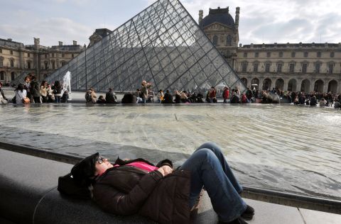 People enjoy sunny spring weather, a break from an unusually cold spring, near the Louvre Pyramid at the Cour Carree of the Louvre Museum on Sunday, April 7, in Paris.