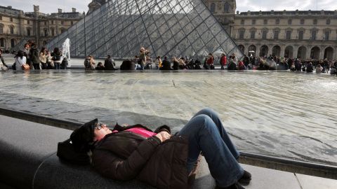 People enjoy sunny spring weather, a break from an unusually cold spring, near the Louvre Pyramid at the Cour Carree of the Louvre Museum on Sunday, April 7, in Paris.