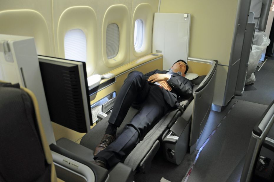 Our fill-in model demonstrates a fully reclined first-class seat. When properly set up for flight, there's a mattress on top of the seat. A partition can be raised between seats to increase privacy. We don't recommend sleeping in a business suit.