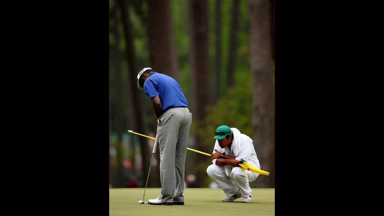 Vijay Singh of Fiji putts as his caddie watches on the third hole.