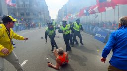 Police officers with their guns drawn hear the second explosion down the street. The first explosion knocked down 78-year-old runner Bill Iffrig at the finish line. He got up a few minutes later and finished the race.