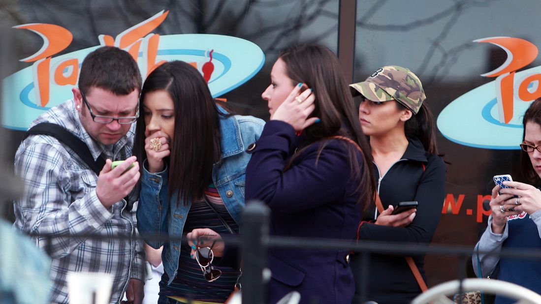 Bystanders check their mobile devices for news of the explosions.