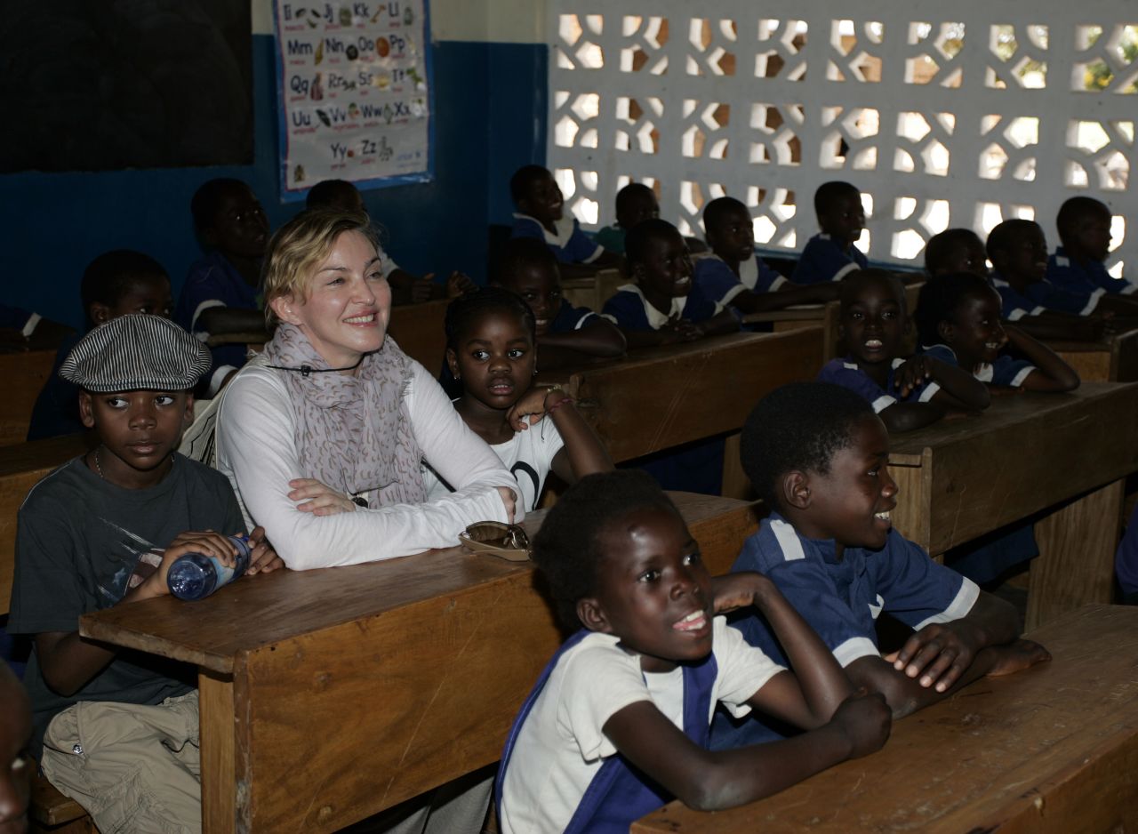 Madonna sinks flanked by the two Malawian children she adopted -- David Banda and Mercy James -- in a classroom at Mkoko Primary School, central Malawi, on April 2, 2013.