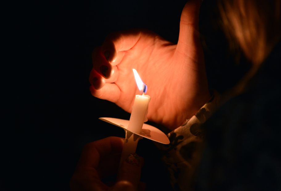 A woman uses her hand to keep wind from her candle during an interfaith service in Boston on April 16, 2013.