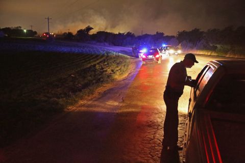 With smoke rising in the distance, a law enforcement officer runs a checkpoint at the perimeter about half a mile from the plant.