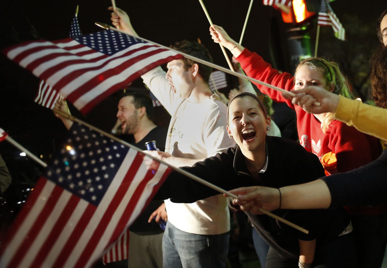 People wave U.S. flags as police drive down the street on April 19.