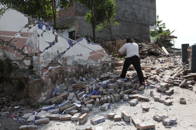 A woman walks on bricks fallen from a collapsed house Saturday in Longmen township.