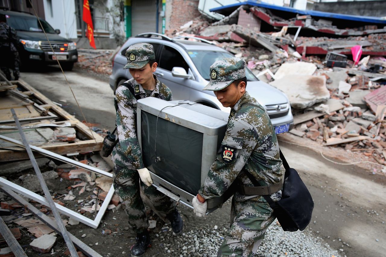 Two soldiers help move a television from a damaged house on Monday in Ya'an.