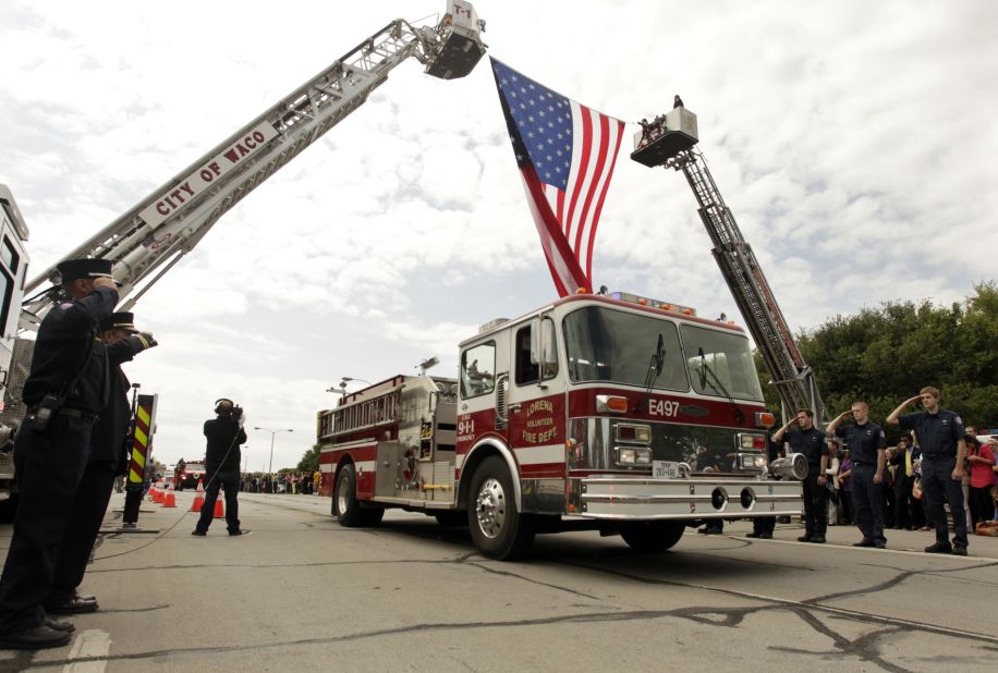 Firefighters salute as fire trucks and emergency vehicles pass under a flag before the memorial service on April 25.