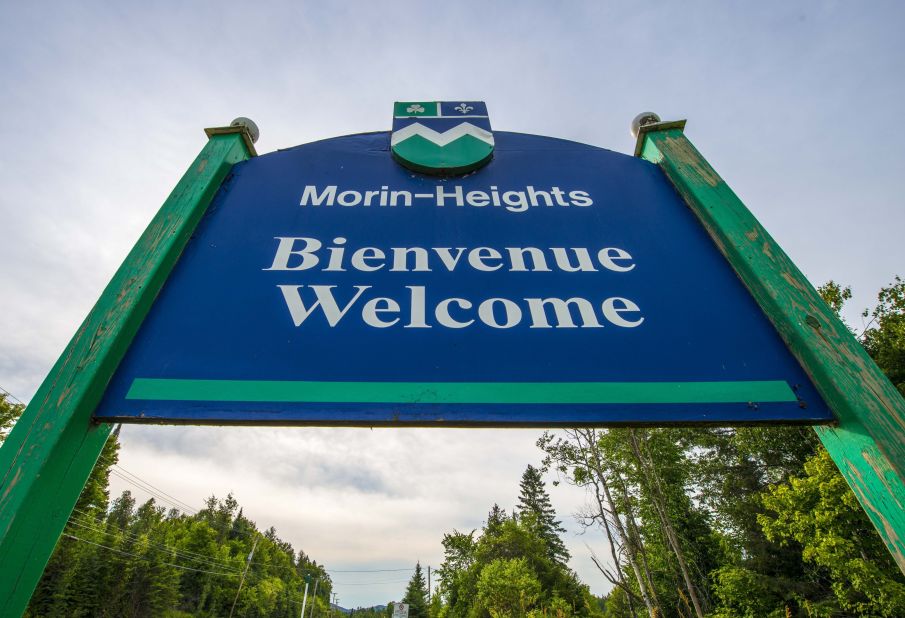 A sign reading "Welcome" in French and English stands at the entrance to Morin-Heights, a tourist town in the Laurentian Mountains region of Quebec, Canada. In Quebec, French must be the predominant language on signs, retail or food service employees always greet customers in French, and there are laws dictating whether parents can send their children to English or French school.