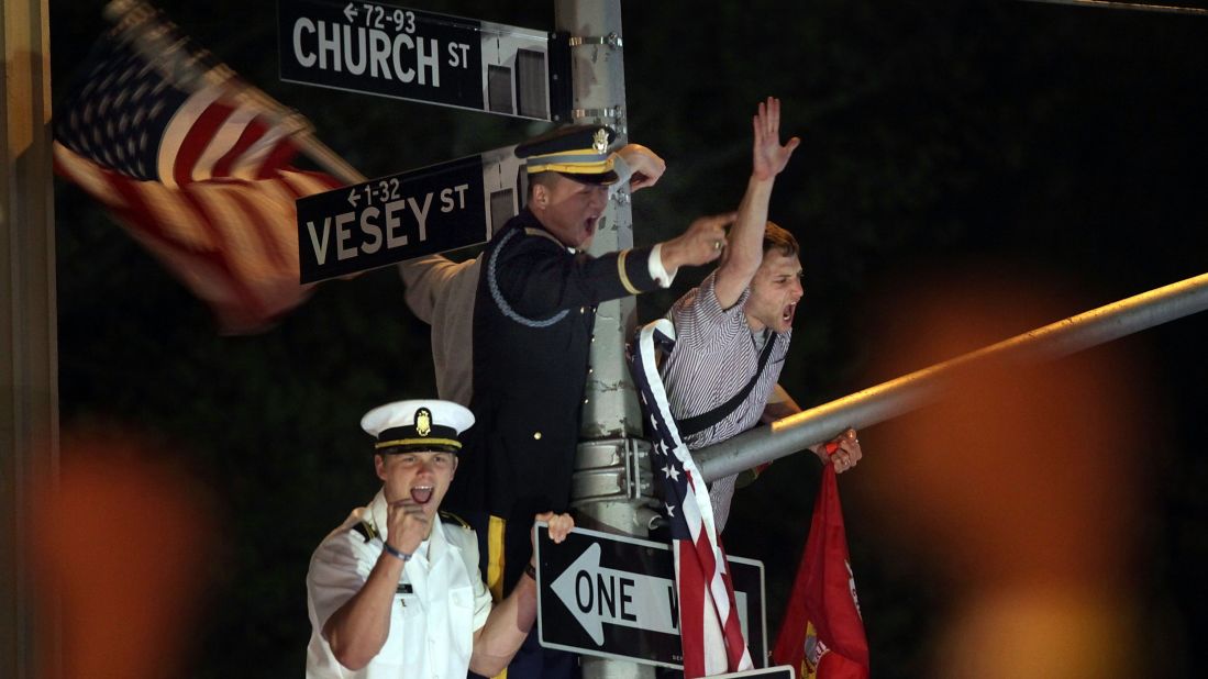 Servicemen cheer from a lamp post as thousands of people gather at Ground Zero in New York City.