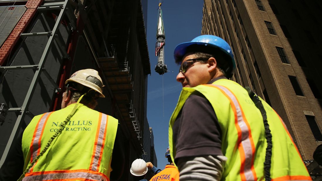 Construction workers watch as the 408-foot spire is hoisted onto a temporary platform on the top of One World Trade Center. 