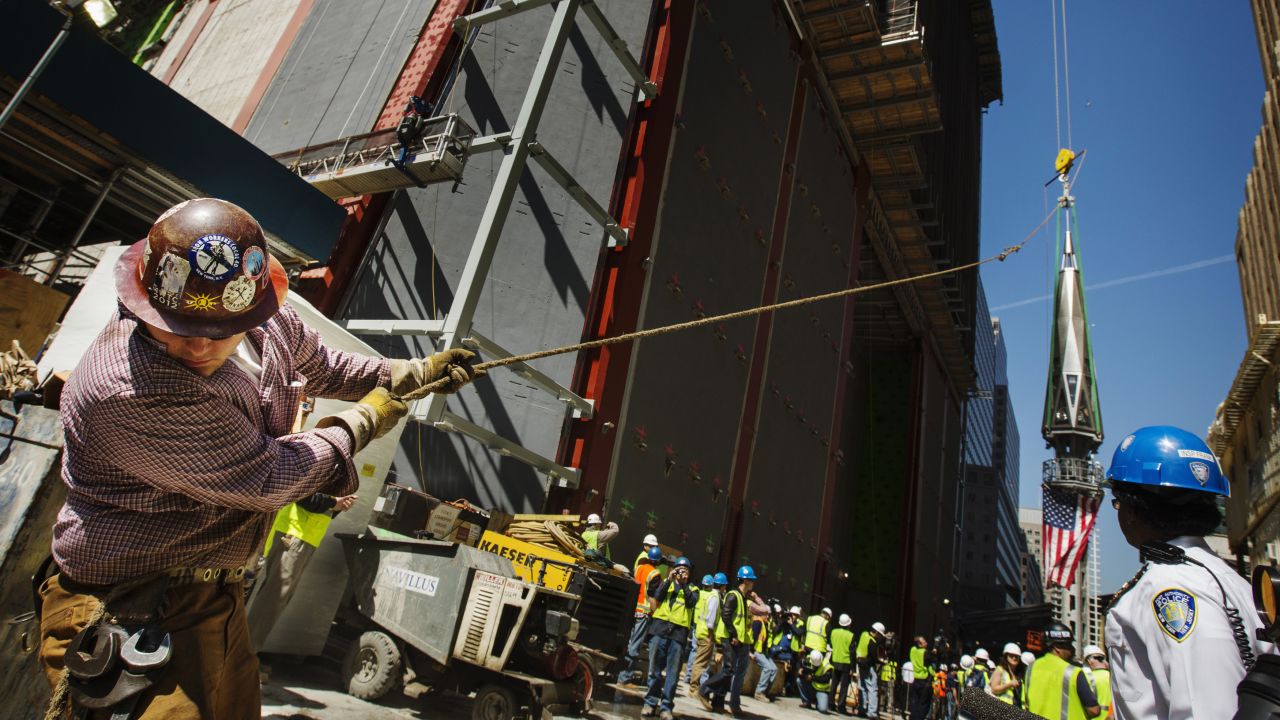 An ironworker uses a line to steady the final piece of the spire.