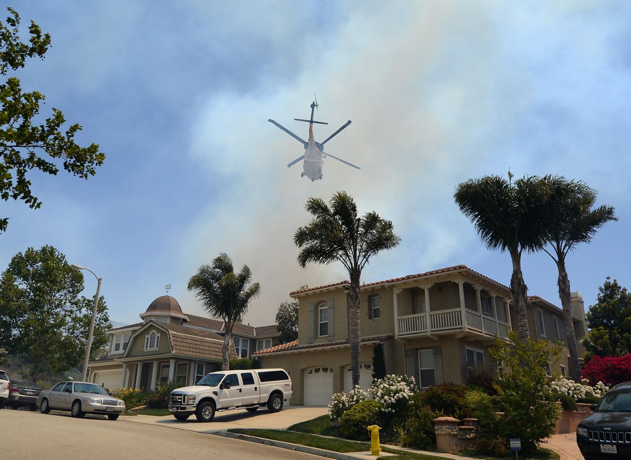 A firefighting helicopter comes in to make a water drop behind homes threatened by the fire on Thursday.  Ninety-six fire engines, six helicopters and five bulldozers have been deployed in battling two California wildfires in the Los Angeles area, according to fire authorities.