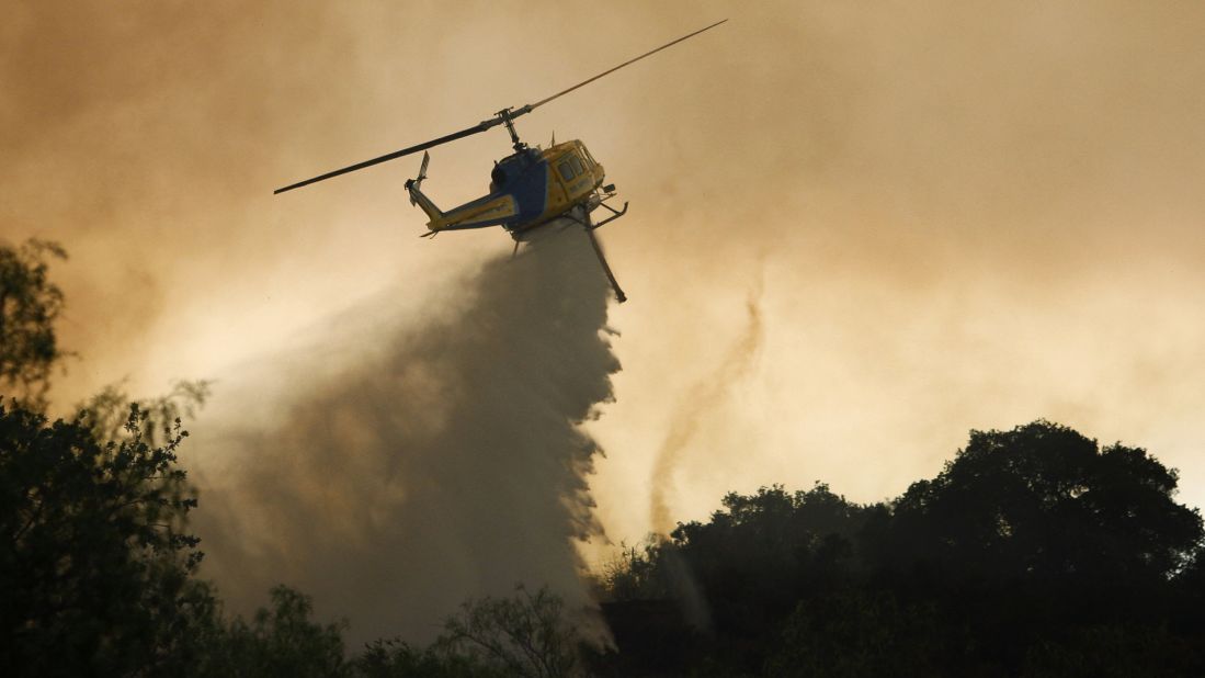 A helicopter makes a water drop next to a small fire tornado near Camarillo.