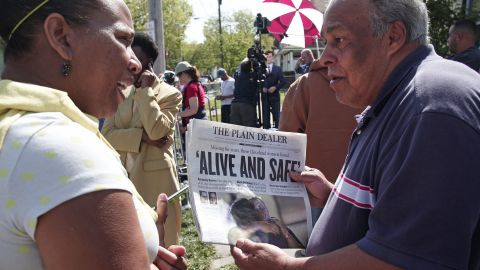 A bystander shows the front page of The Plain Dealer newspaper to a friend outside of the house on Seymour Avenue on May 7.
