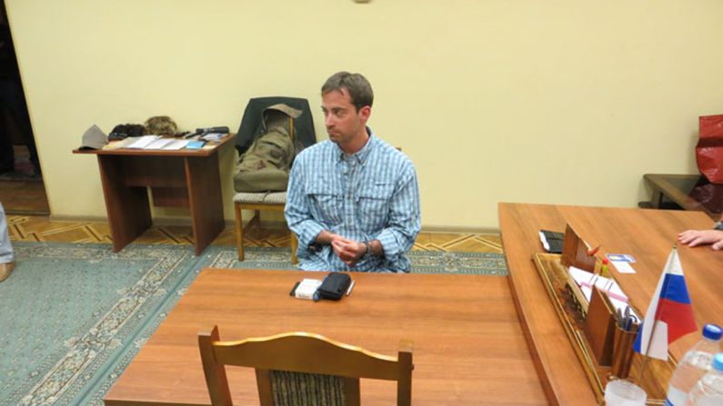 The man sits behind a desk after being detained.