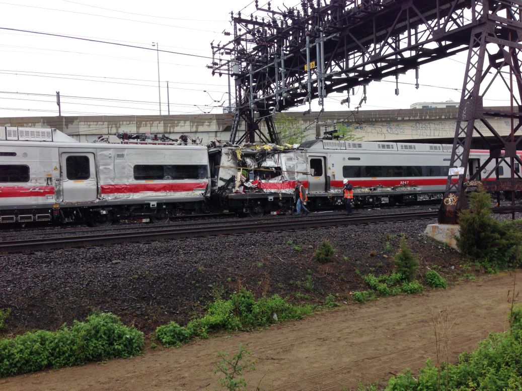 Investigators walk past two train cars damaged in the collision on Friday, May 17.