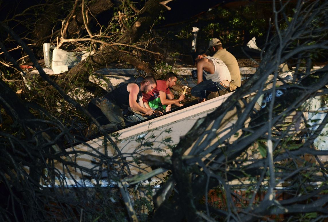 Residents repair the roof of a neighbor's damaged house after a tree fell on it in Shawnee on May 19.