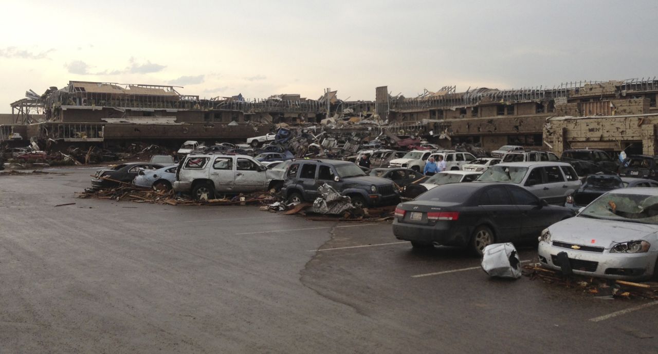A shopping center parking lot is covered with debris and damaged cars on May 20.