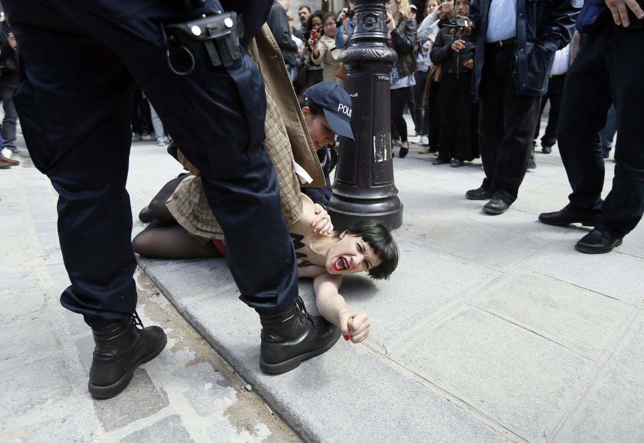 A member of the FEMEN feminist activist group with writing on her chest reading "May fascists rest in hell" is arrested by police officers after taking part in a protest at Notre Dame Cathedral in Paris on Wednesday, May 22.  The protesters were demonstrating against the suicide of a far-right activist inside the cathedral the previous day.