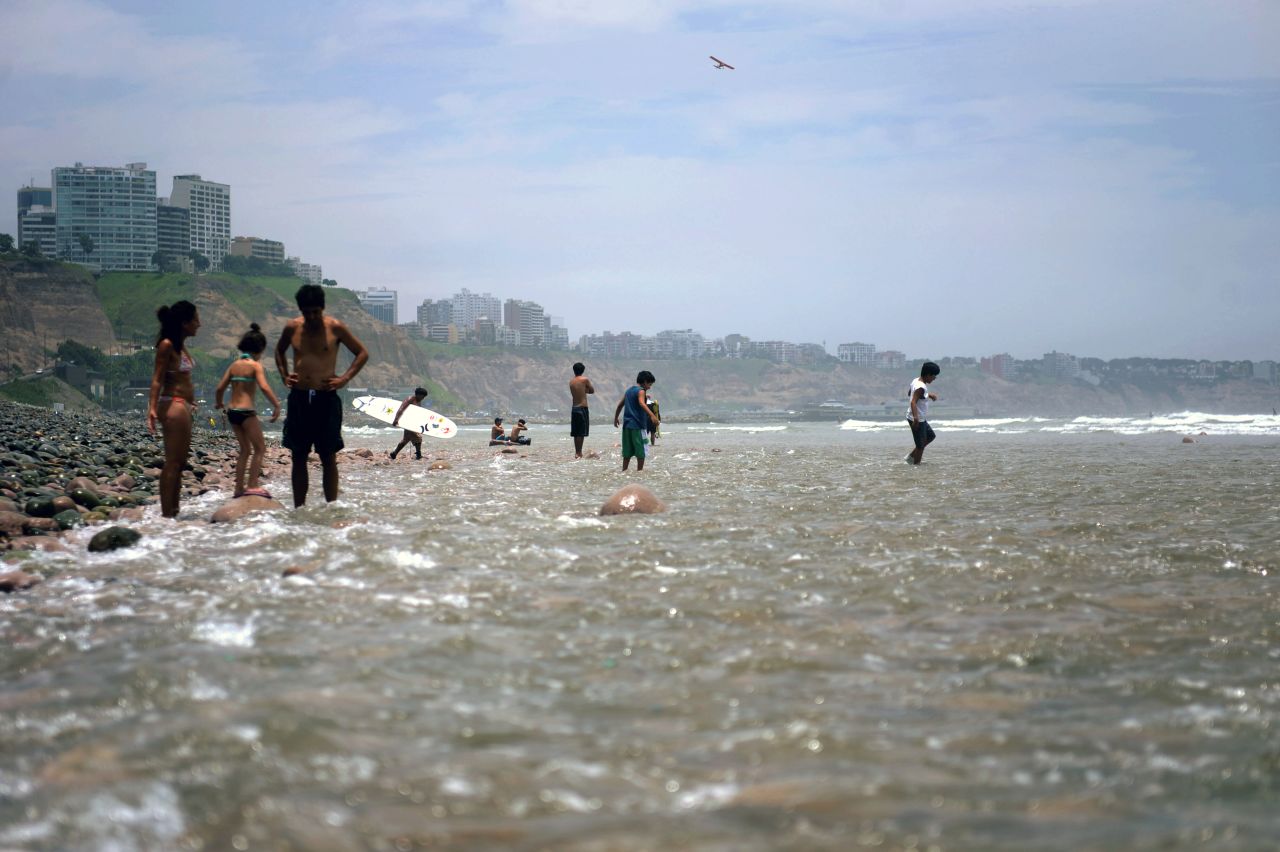 People wade in the water at a beach in Lima.