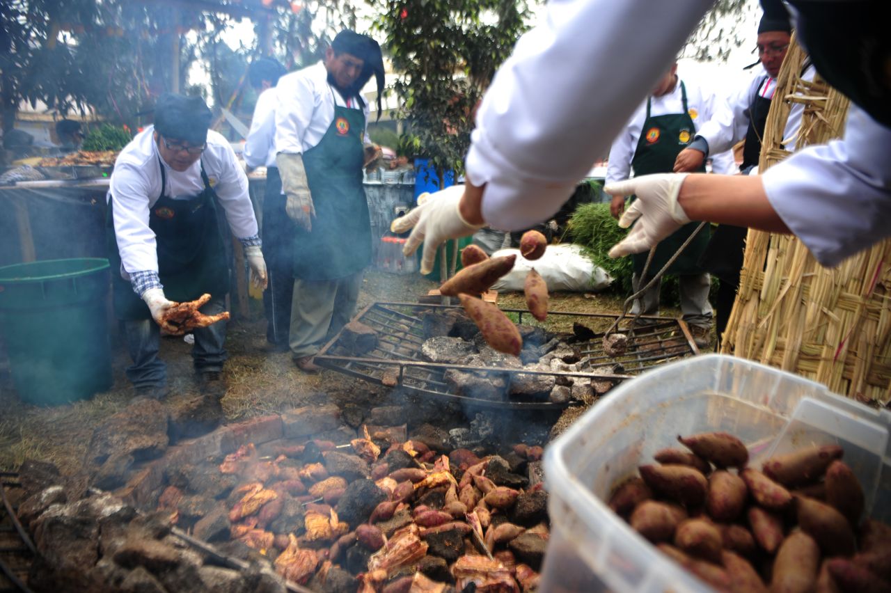 People throw potatoes into a pachamanca, a traditional Peruvian dish cooked on hot stones.