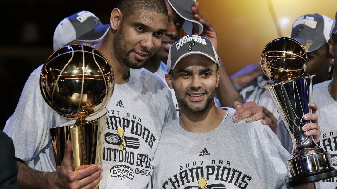 Duncan poses with the NBA Championship Larry O'Brien Trophy while teammate Tony Parker hoists the MVP Trophy after leading the Spurs to their fourth NBA title with their 2007 sweep of the Cleveland Cavaliers.