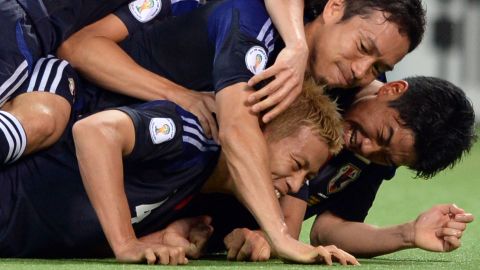 Japan's Keisuke Honda is mobbed by his teammates after scoring a 91st-minute penalty.